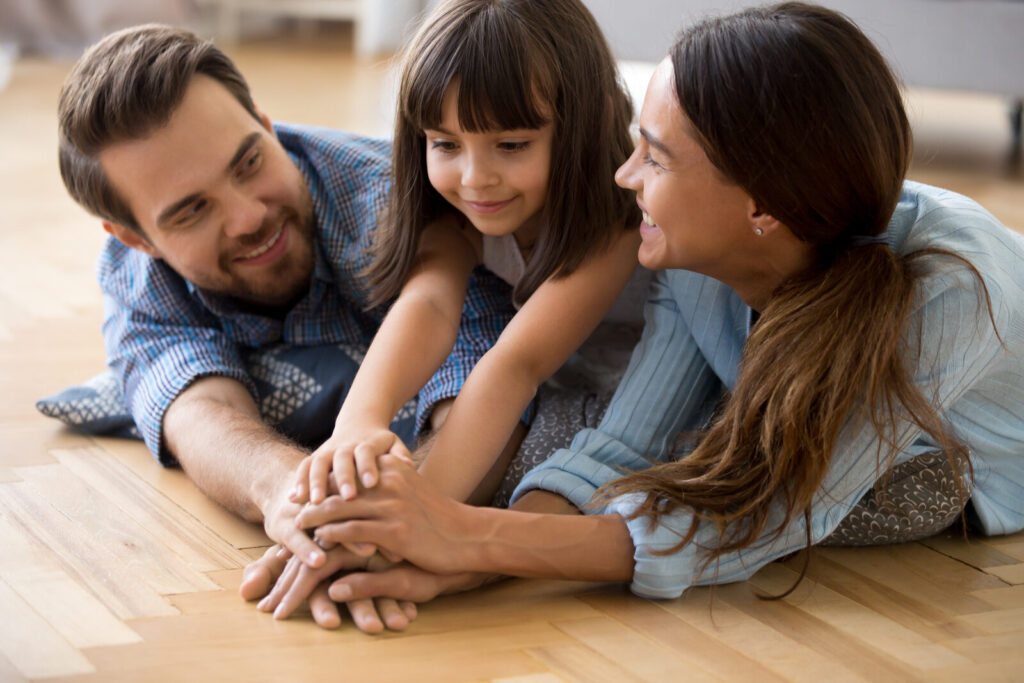 Pai, mãe e filha unindo as mãos em ambiente acolhedor